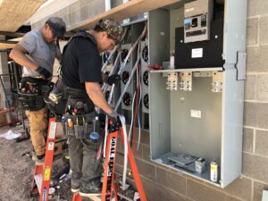Two electricians installing an outdoor electrical meter bank for a commercial property by Goal Electric LLC in West Valley City, UT.