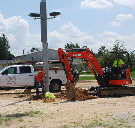 Electricians installing an outdoor light pole or electrical infrastructure with an excavator for Triple T Electric in Cedarburg, WI.