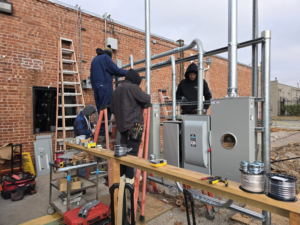 Electricians installing an outdoor electrical service panel and conduits on a brick building for Hummingbird Electric Inc. in Tulsa, OK.