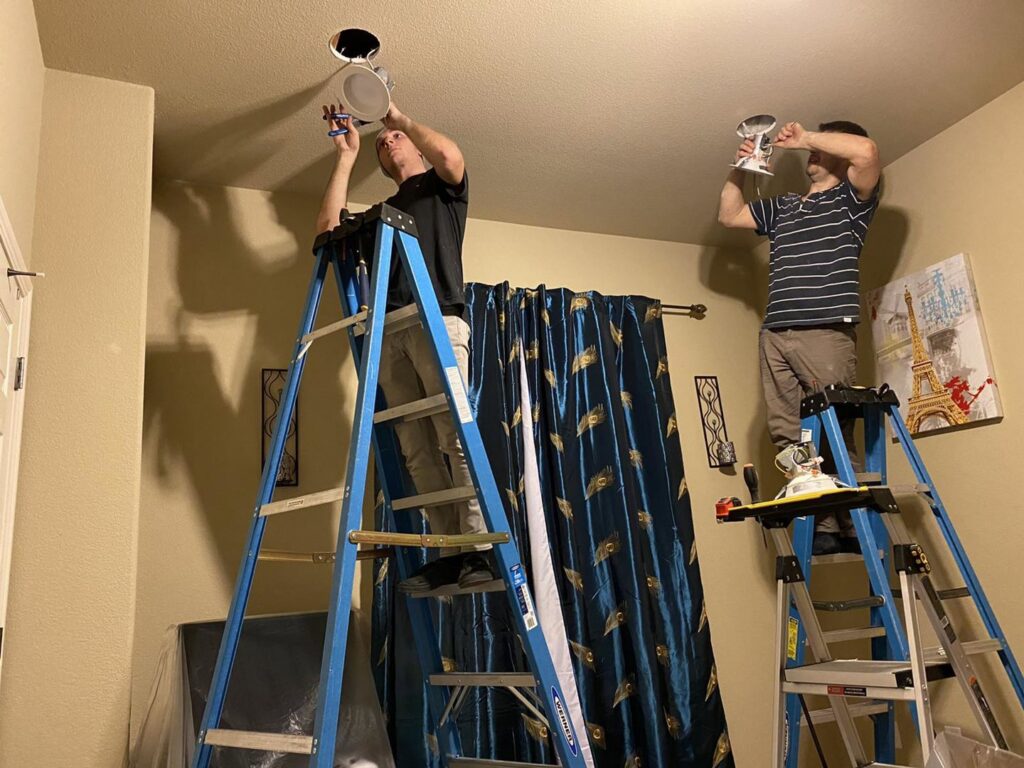 Two electricians on ladders installing recessed lighting in a home, a service from Vitality Electric in Sacramento, CA.