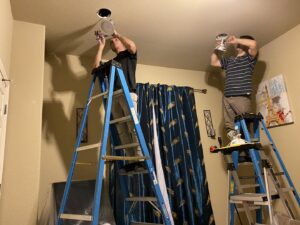 Two electricians on ladders installing recessed lighting in a home, a service from Vitality Electric in Sacramento, CA.