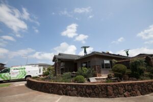 Electricians from Alternate Energy Inc. installing solar panels on a roof, with a company van visible in Pearl City, HI.