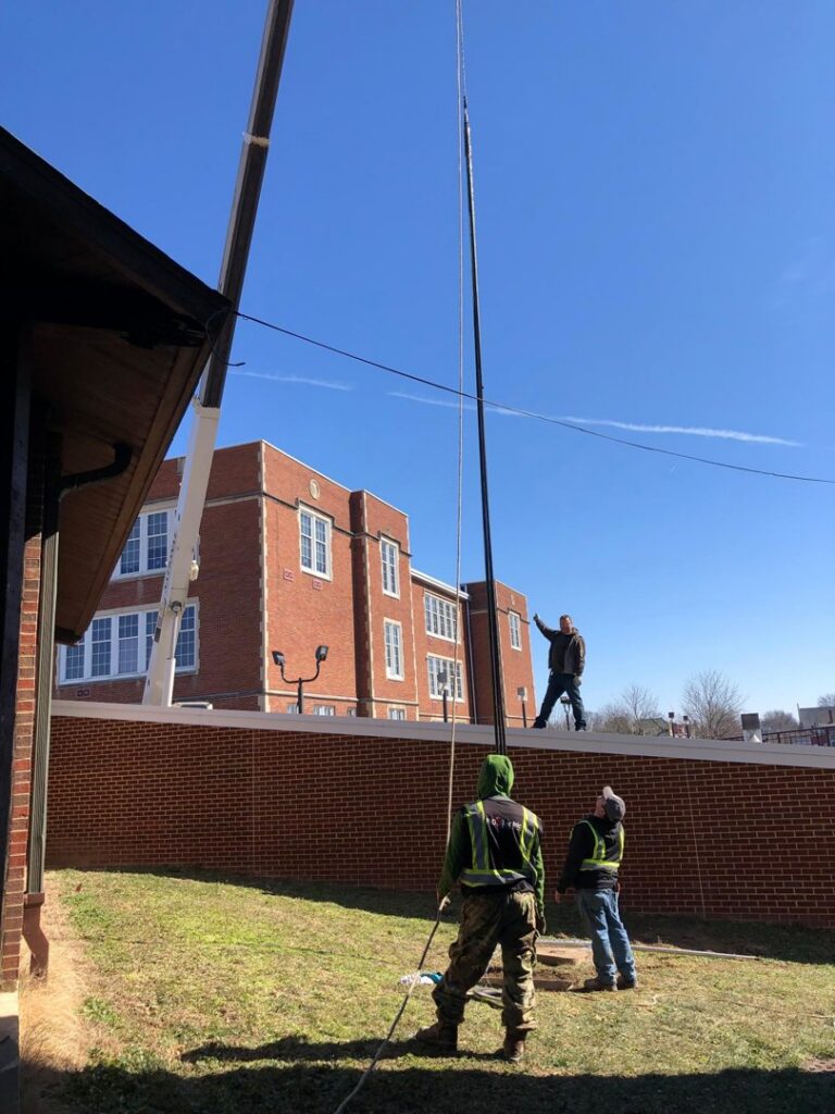 Electricians installing a tall pole with a crane at a commercial site by Pro 1 Electric, Inc. in Parkersburg, WV
