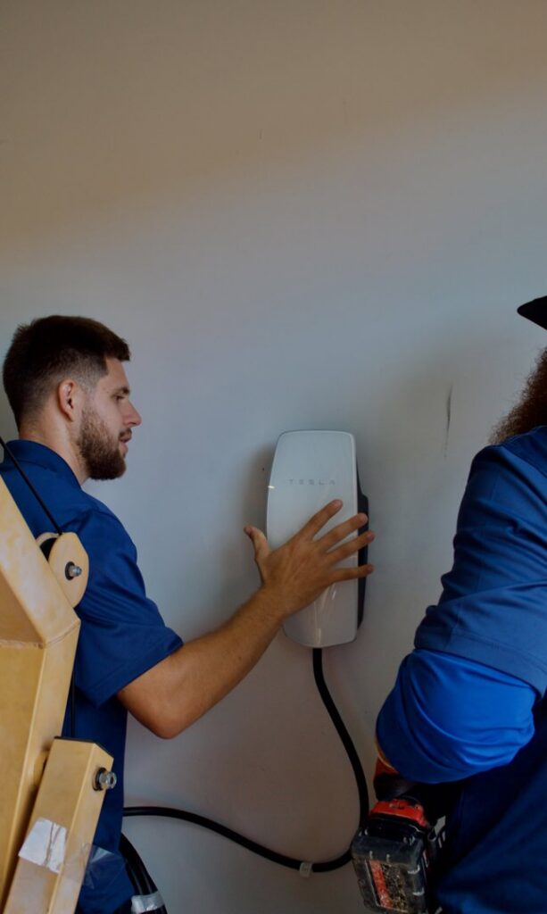 Two electricians installing a Tesla EV charger on a wall, provided by Miller and Sons Electric in North Myrtle Beach, SC.