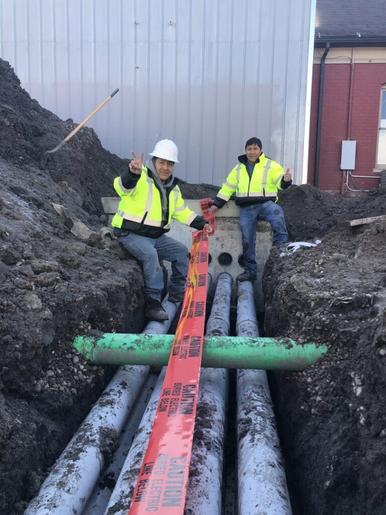Electricians installing underground electrical conduit in a trench for Goal Electric LLC in West Valley City, UT.