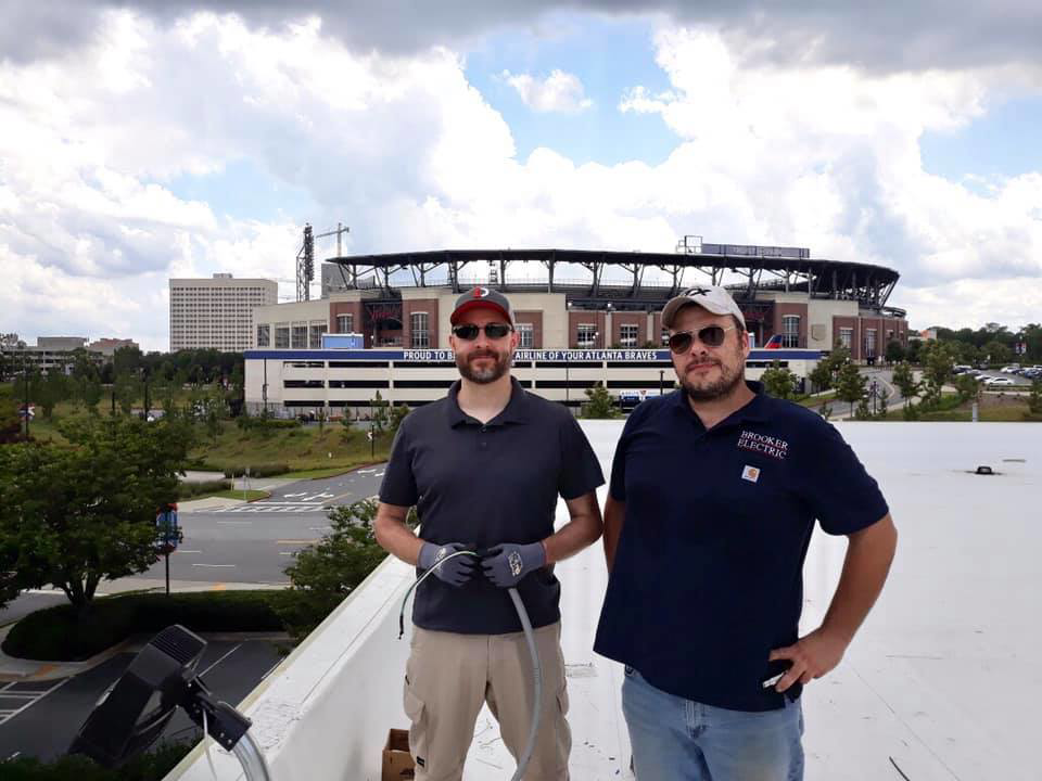 Two electricians from Brooker Electric in Roswell, GA, on a rooftop, one holding electrical conduit, ready for an installation or repair.