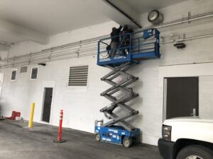 Electricians on a scissor lift installing overhead electrical conduit for Goal Electric LLC in West Valley City, UT.