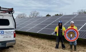 Two electricians in safety gear standing in front of a large solar panel array for IBEW Local 24 Membership Development in Baltimore, MD.