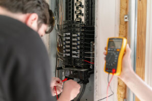 Two electricians using a multimeter to test an electrical panel for Common Ground Electrical in Baltimore, MD.