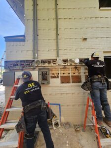 Two electricians from Acevedo's Electric upgrading outdoor electrical meters and panels on a commercial building in Dallas, TX.
