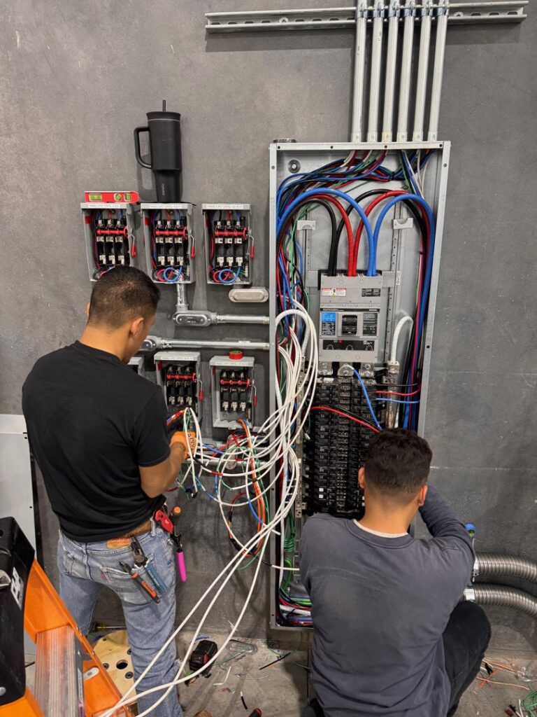 Two electricians actively wiring a large commercial electrical panel for Industrial Edge Electrical in Gilbert, AZ.