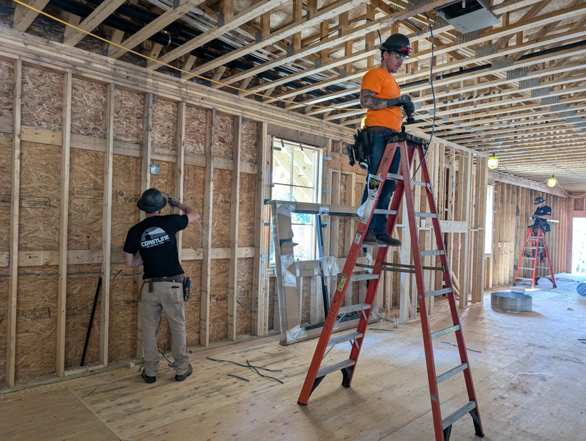 Two electricians from coastline.electric.inc installing new wiring in a residential construction project in Boston, MA.