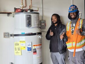 Two Muse Electricians giving thumbs up next to a newly installed water heater in Los Angeles, CA, showcasing completed work.