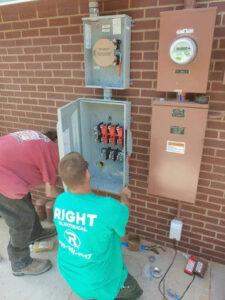 Two electricians from Right Electrical Services LLC working on an exterior electrical panel and meter base in Raleigh, NC.