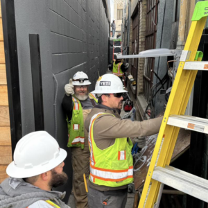 Electricians in hard hats and safety vests working with ladders in a narrow alleyway for Wheeler Electric, Inc. in Idaho Falls, ID.