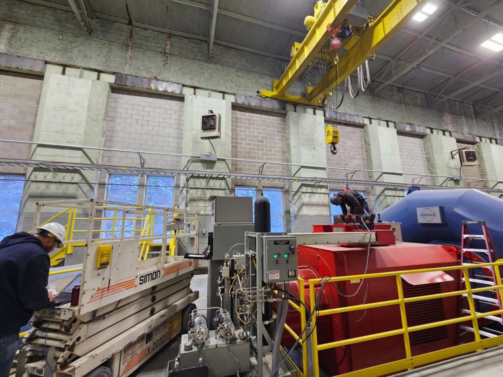 Two electricians working on industrial machinery in a large facility, one using a scissor lift, for Trademark Elite Electrical Services in Butte, MT