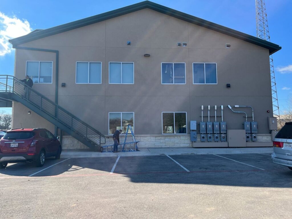 Electricians working on exterior electrical panels and conduits at a commercial building for All American Pro Electric LLC in Cedar Creek, TX.