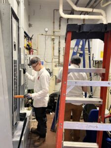 Two electricians working on commercial electrical panels in a utility room for Buckeye Electric of Upper Arlington, LLC in Columbus, OH.