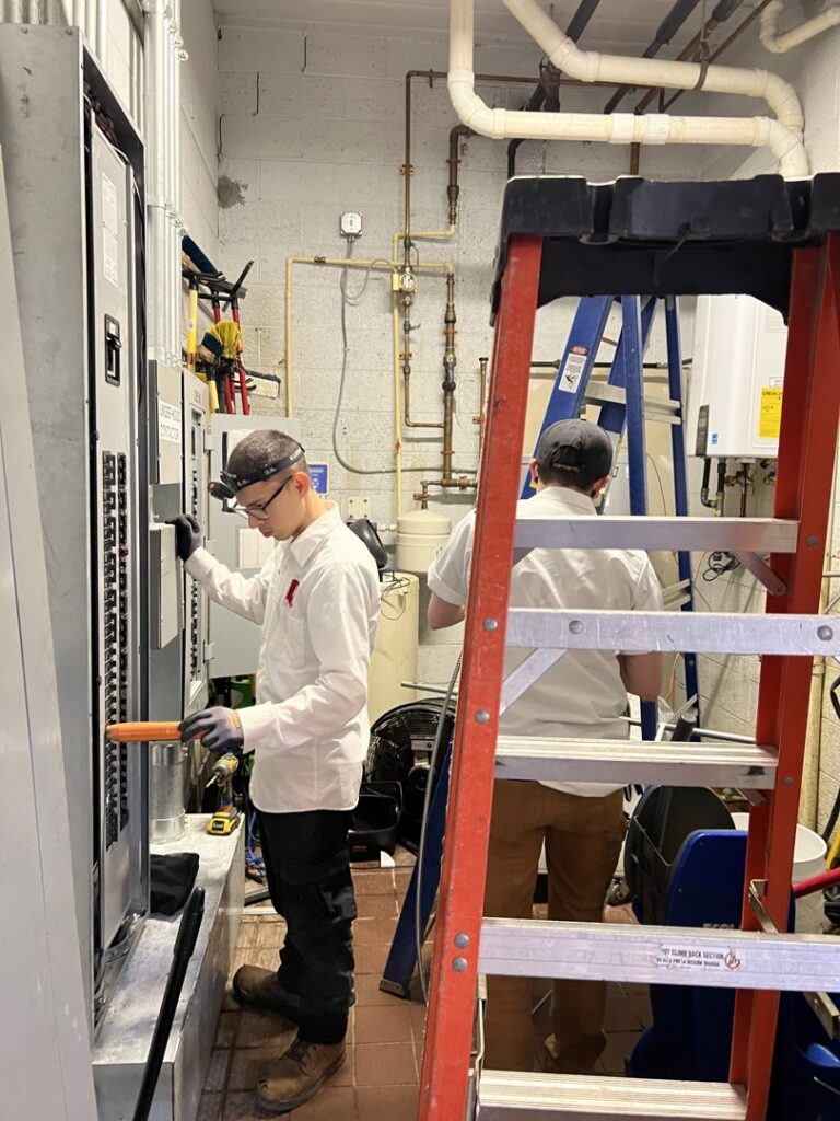 Two electricians working on commercial electrical panels in a utility room for Buckeye Electric of Upper Arlington, LLC in Columbus, OH.