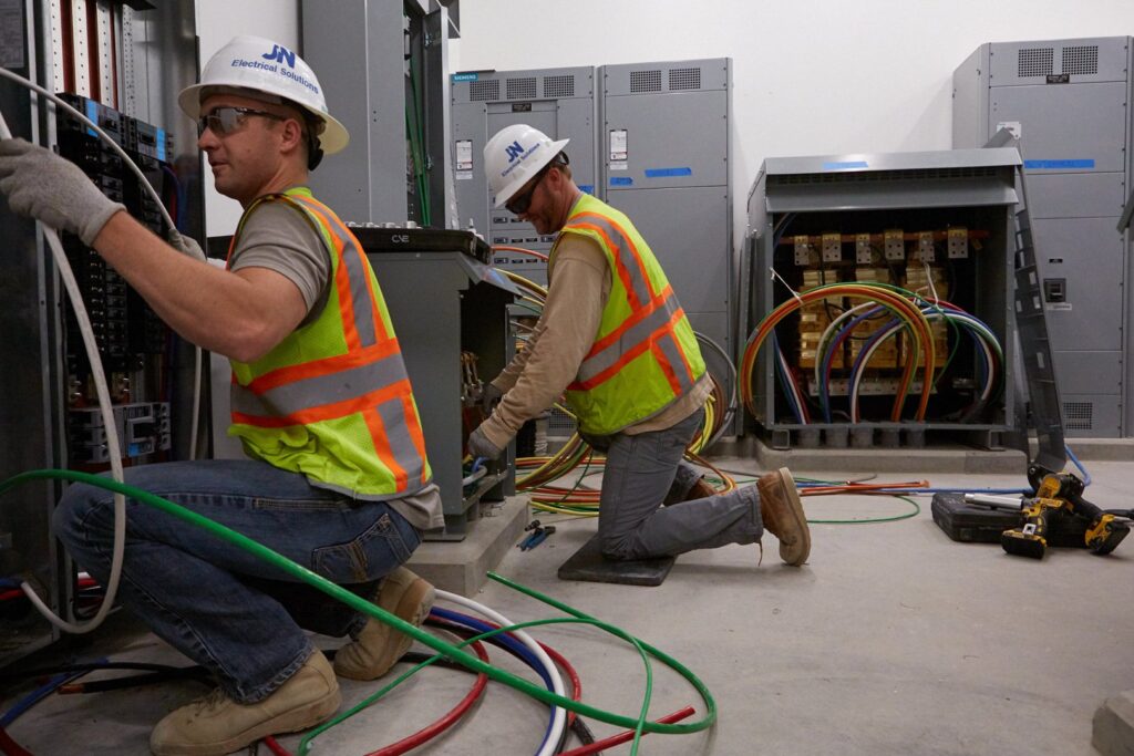 Two electricians in safety gear working on commercial electrical panels for JN Electrical Solutions in Hopewell, PA.