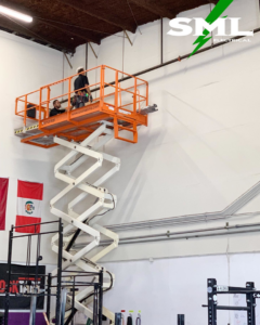 Two electricians on a scissor lift platform, actively working on electrical conduit and wiring at height for SML Electrical in Pearl City, HI.