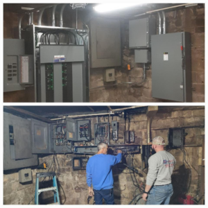 Two electricians working on multiple electrical panels and wiring in a utility room for Boyd Electric, LLC in Evansville, IN