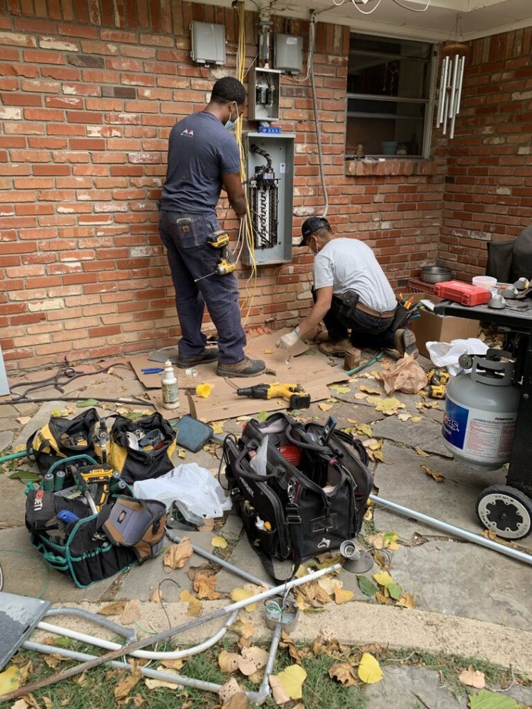 Two electricians from AVA Electric, LLC working on an exterior electrical panel and wiring in Fort Worth, TX.