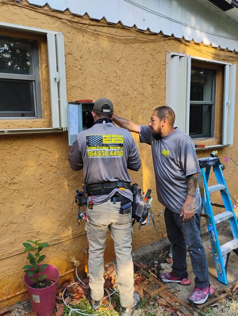 Two electricians from Envision Electrical Solutions working on an exterior electrical panel on a house in Fort Lauderdale, FL.