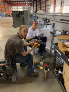 Two Diamond Electric electricians working on industrial electrical equipment in a warehouse in Toledo, OH.