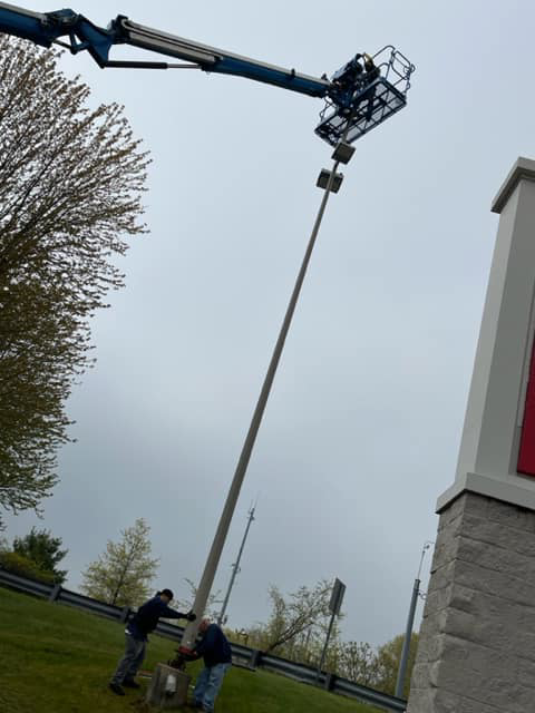 Electricians working at the base of a tall light pole with a boom lift from Lighting Services, Inc. in Waterbury, CT.