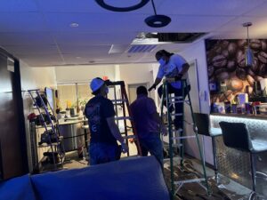 Electricians on ladders working on an office ceiling installation or repair for Llanos Electric Builders in Houston, TX.