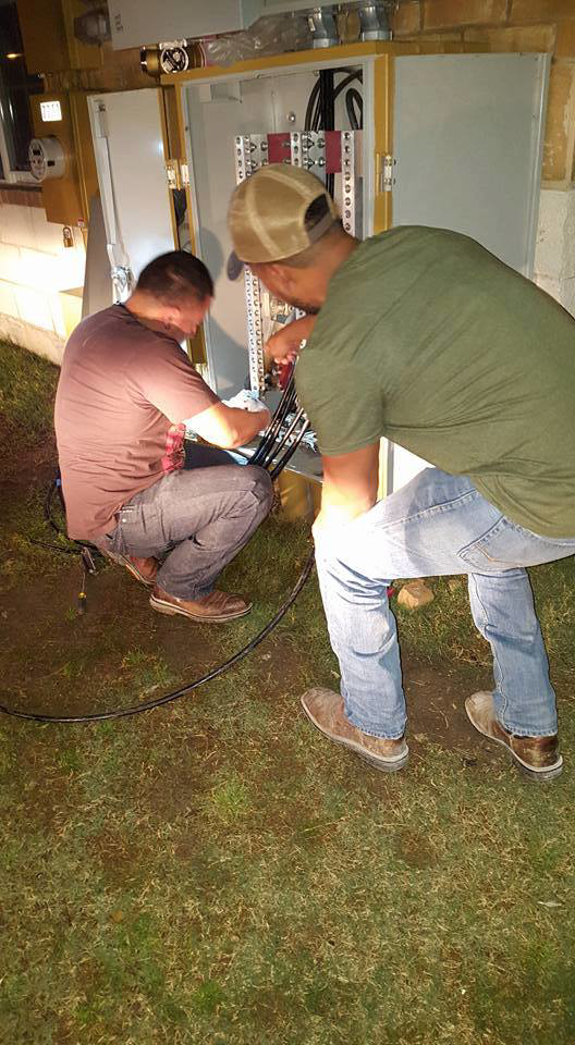 Two electricians working on an outdoor electrical panel at night for Genesys Electrical Contractors in Dallas, TX