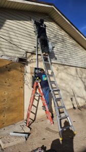Two electricians from V Electrical LLC working on an outdoor electrical panel and service mast in Albuquerque, NM.
