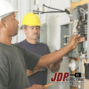 Two electricians in hard hats working on an electrical panel at JDP Electric in Fargo, ND.
