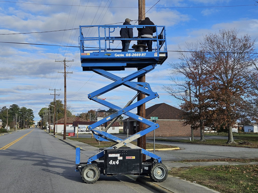 Two electricians working on a utility pole from a scissor lift, performing electrical service for Jernigan Electrical Service Co., LLC in Windsor, NC.