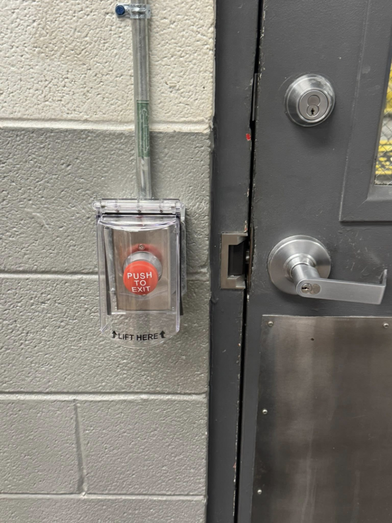 A professionally installed emergency 'PUSH TO EXIT' button with electrical conduit next to a commercial door by Flash Construction in Winifrede, WV.
