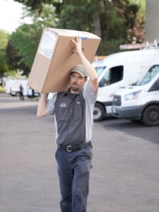 An employee carrying a large box of HVAC equipment for Specialty Heating and Cooling in Portland, OR.