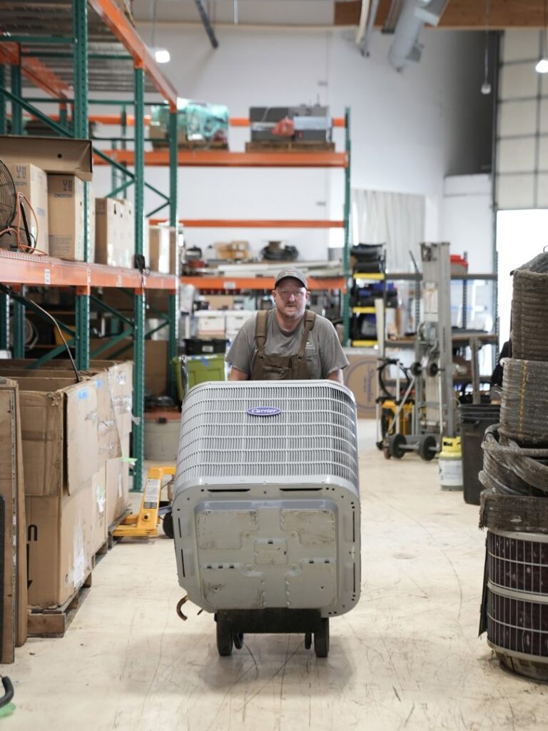An employee moving an outdoor air conditioning unit on a dolly for Specialty Heating and Cooling in Portland, OR.