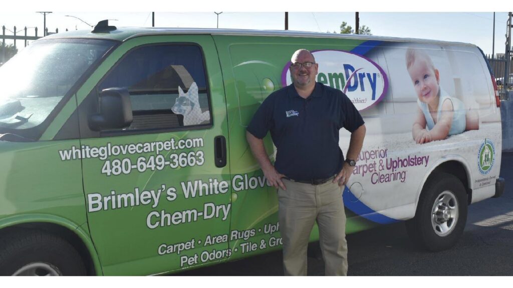 An employee stands proudly next to a Brimley's White Glove Chem-Dry service van in Mesa, AZ, ready for carpet cleaning.