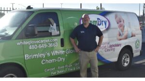 An employee stands proudly next to a Brimley's White Glove Chem-Dry service van in Mesa, AZ, ready for carpet cleaning.