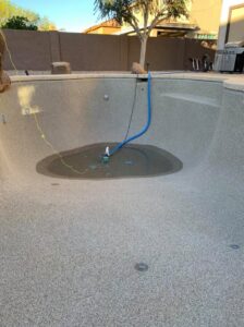 An empty pool with a drainage pump and hose at the bottom, illustrating pool draining services by Space Ranger Pools in Gilbert, AZ.
