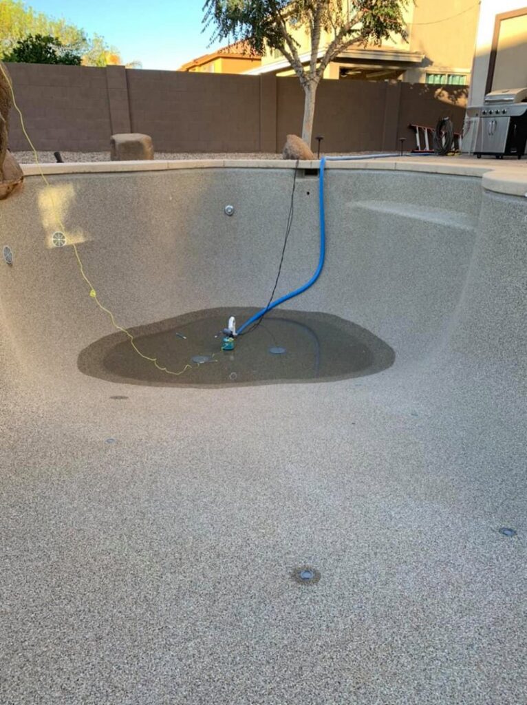 An empty pool with a drainage pump and hose at the bottom, illustrating pool draining services by Space Ranger Pools in Gilbert, AZ.
