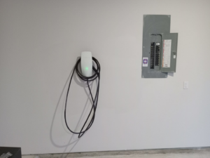 An installed EV charger and open electrical panel in a garage by Valle Home Maintenance in Houston, TX
