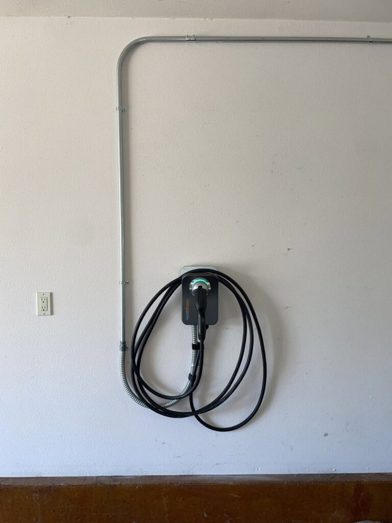 An EV charger with electrical conduit installed along a garage wall by Delatour Electric in Portland, OR.
