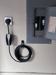 An electric vehicle charger connected near an open electrical panel, demonstrating installation services by Quistian Lighting in Arlington, TX