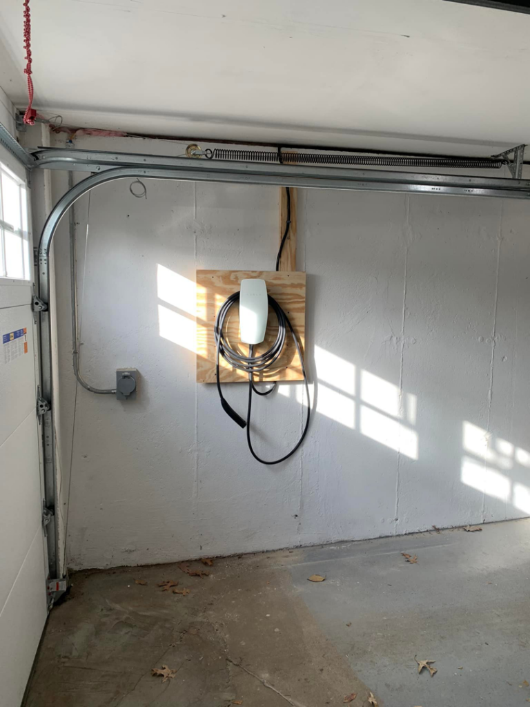 An installed Tesla EV charger in a garage, a service provided by Benoit Electrical Services in Litchfield, NH.