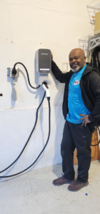An electrician from Lake Electric Maine in Biddeford, ME, stands next to a newly installed EV charging station.
