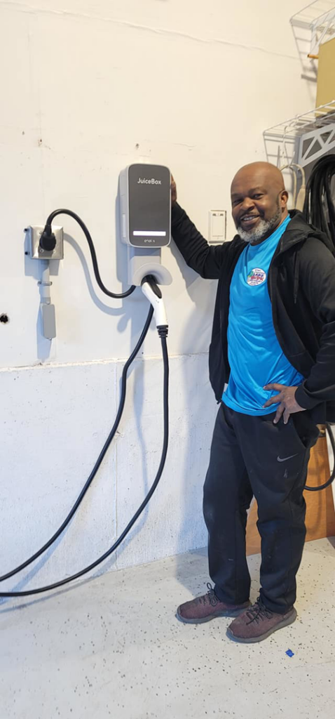 An electrician from Lake Electric Maine in Biddeford, ME, stands next to a newly installed EV charging station.