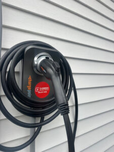 An EV charging station installed on the white siding of a home by Clemens Electric in Averill Park, NY