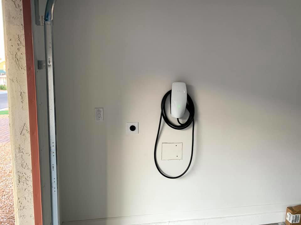 An installed Tesla EV charger and electrical outlet on a garage wall by R&M Electric LLC in Gilbert, AZ.